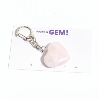 One of the five soft pink rose quartz heart charms from the pack, shown on its "you're a GEM!" gift backing card, hanging from its silver clasp on a clean white background. Stonebridge Imports.