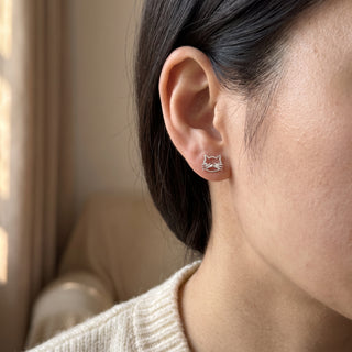 925 Silver Cat Earrings worn on the earlobe in soft natural light, showing the polished sterling silver cat-face stud at true scale.