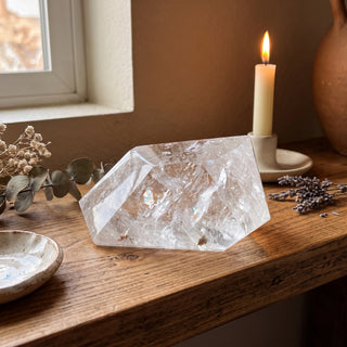 Clear Quartz Free Form Unique #1 displayed on a wooden home altar shelf beside a candle, shown at true size in warm natural light.
