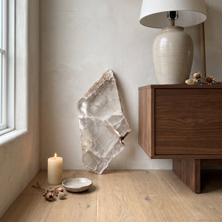 Selenite Window Slab Unique #19 - 17" displayed leaning against a wall on a light oak floor beside a lit candle, shown at true size in warm natural light.