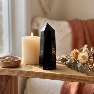 Black Obsidian Generator displayed on a wooden home altar shelf beside a lit candle and dried botanicals, shown at true size in warm natural light.