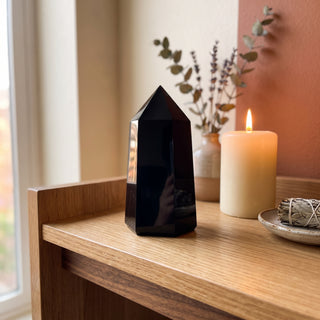Black Obsidian Generator Unique #3 displayed on a wooden home altar shelf beside a lit candle and dried botanicals, shown at true size in warm natural light.