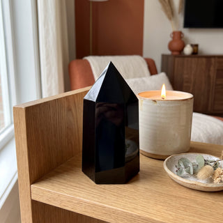 Black Obsidian Generator Unique #8 displayed on a wooden home altar shelf beside a lit candle and dried botanicals, shown at true size in warm natural light.