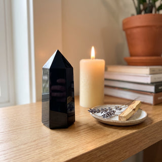Black Obsidian Generator Unique #13 displayed on a wooden home altar shelf beside a lit candle and dried botanicals, shown at true size in warm natural light.