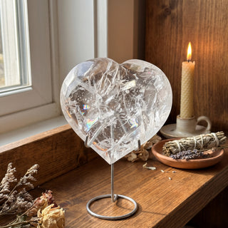 Clear Quartz Heart on Stand Unique #2 displayed on a wooden home altar shelf beside a candle, shown at true size in warm natural light.