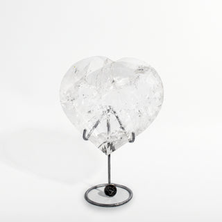Clear Quartz Heart on Stand Unique #2, a polished clear quartz heart on a silver metal stand shown from an alternate angle on a clean white background. Stonebridge Imports.