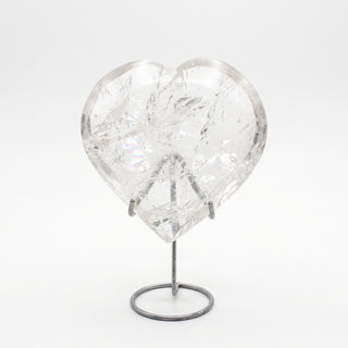 Clear Quartz Heart on Stand Unique #2, a polished clear quartz heart on a silver metal stand shown from an alternate angle on a clean white background. Stonebridge Imports.