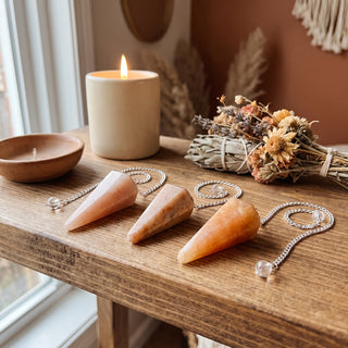 Peach Aventurine Pendulum 6 Facet & Bead - 3 Pack on a wooden altar shelf beside a candle, three peach aventurine pendulums at true size in warm natural light.