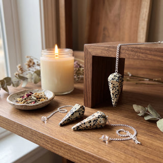 Dalmatian Jasper Pendulum 6 Facet & Bead - 3 Pack on a wooden altar shelf beside a candle, three spotted Dalmatian jasper pendulums at true size in warm natural light.