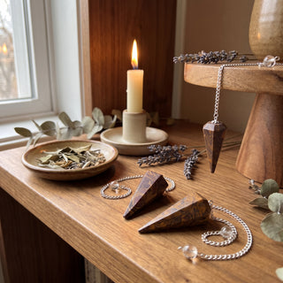 Snake Jasper Pendulum 6 Facet & Bead - 3 Pack on a wooden altar shelf beside a candle, three swirled snake jasper pendulums at true size in warm natural light.