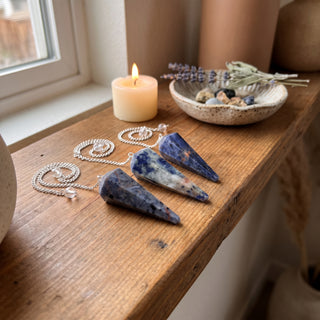 Sodalite Pendulum 6 Facet & Bead - 3 Pack on a wooden altar shelf beside a candle, three deep blue sodalite pendulums at true size in warm natural light.