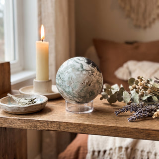 Green Tree Agate Sphere displayed on a wooden home altar shelf beside a candle, resting on a clear display ring, shown at true size in warm natural light.