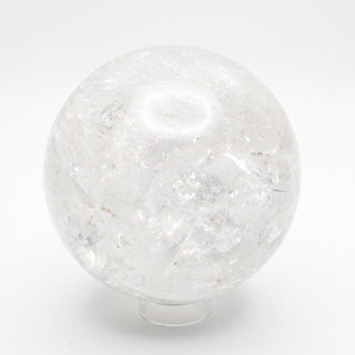 Clear Quartz Sphere Unique #19 - 6", a polished clear quartz sphere on a clear display stand shown from an alternate angle on a clean white background. Stonebridge Imports.