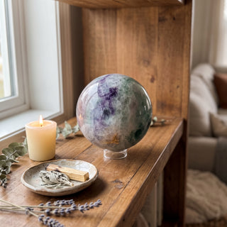 Fluorite Green and Purple Sphere Unique #12 displayed on a wooden home altar shelf beside a candle, shown at true size in warm natural light.
