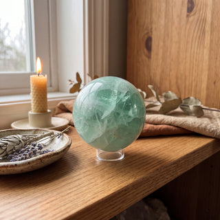 Fluorite Green and Purple Sphere Unique #16 displayed on a wooden home altar shelf beside a candle, shown at true size in warm natural light.