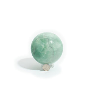 Fluorite Green and Purple Sphere Unique #16 photographed beside a coin for scale, showing the 3" mint-green fluorite sphere on a clean white background. Stonebridge Imports.