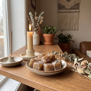 Honey Calcite Tumbled Stones - India heaped in a small ceramic dish on a wooden home altar shelf beside a candle, shown at true size in warm natural light.