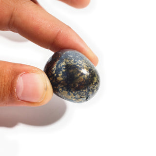 Extra Large — Covellite Tumbled Stones, one large stone dense with gold pyrite flecks held between thumb and finger for scale, photographed on a clean white background. Stonebridge Imports.