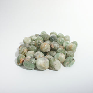 Medium — Green Fluorite Tumbled Stones - India, a pile of soft sea-green and pale green tumbled fluorite with rust flecks, photographed on a clean white background. Stonebridge Imports.