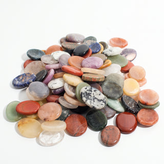 Mixed Stone Worry Stones 100-Pack, a heaped assortment of polished oval thumb stones in mixed crystal colours shown from a low angle on a clean white background. Stonebridge Imports.