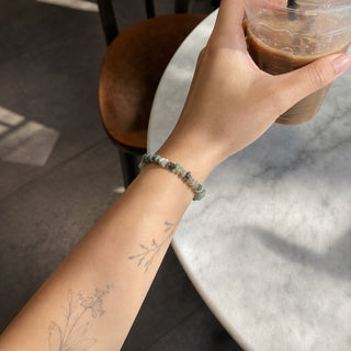 Moss Agate bead bracelet worn on a tattooed forearm holding a coffee