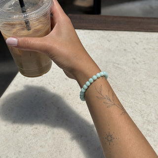 Amazonite bead bracelet worn on a tattooed forearm holding a coffee
