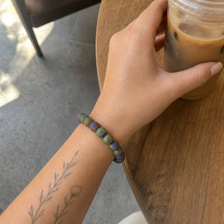 Rainbow Druzy Agate bead bracelet worn on a tattooed forearm holding a coffee
