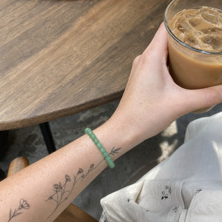 Green Aventurine bead bracelet worn on a tattooed forearm holding a coffee