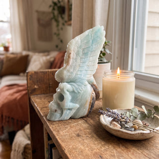 Amazonite Bird Skull Carving Unique displayed on a wooden home altar shelf beside a candle, shown at true size in warm natural light.