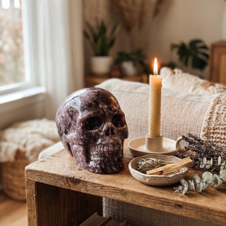 Lepidolite Skull Carving Unique #9 displayed on a wooden home altar shelf beside a candle, shown at true size in warm natural light.