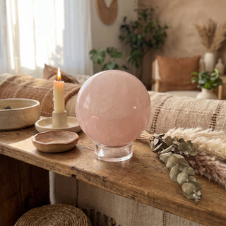 Rose Quartz Sphere Unique #39 - 3 3/8" displayed on a wooden home altar shelf beside a candle, shown at true size in warm natural light.