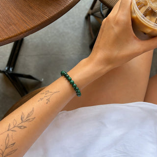 Malachite bead bracelet worn on a tattooed forearm holding a coffee