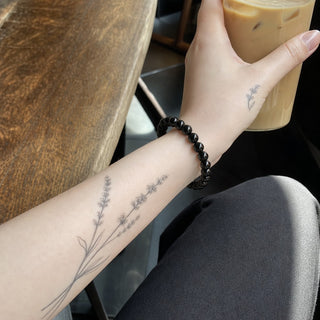 Rainbow Obsidian bead bracelet worn on a tattooed forearm holding a coffee