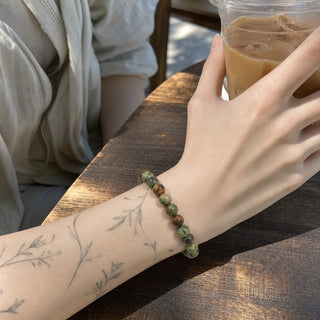 Opal bead bracelet worn on a tattooed forearm holding a coffee