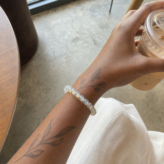 Opalite bead bracelet worn on a tattooed forearm holding a coffee