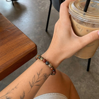 Picasso Jasper bead bracelet worn on a tattooed forearm holding a coffee