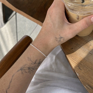 White Moonstone bead bracelet worn on a tattooed forearm holding a coffee